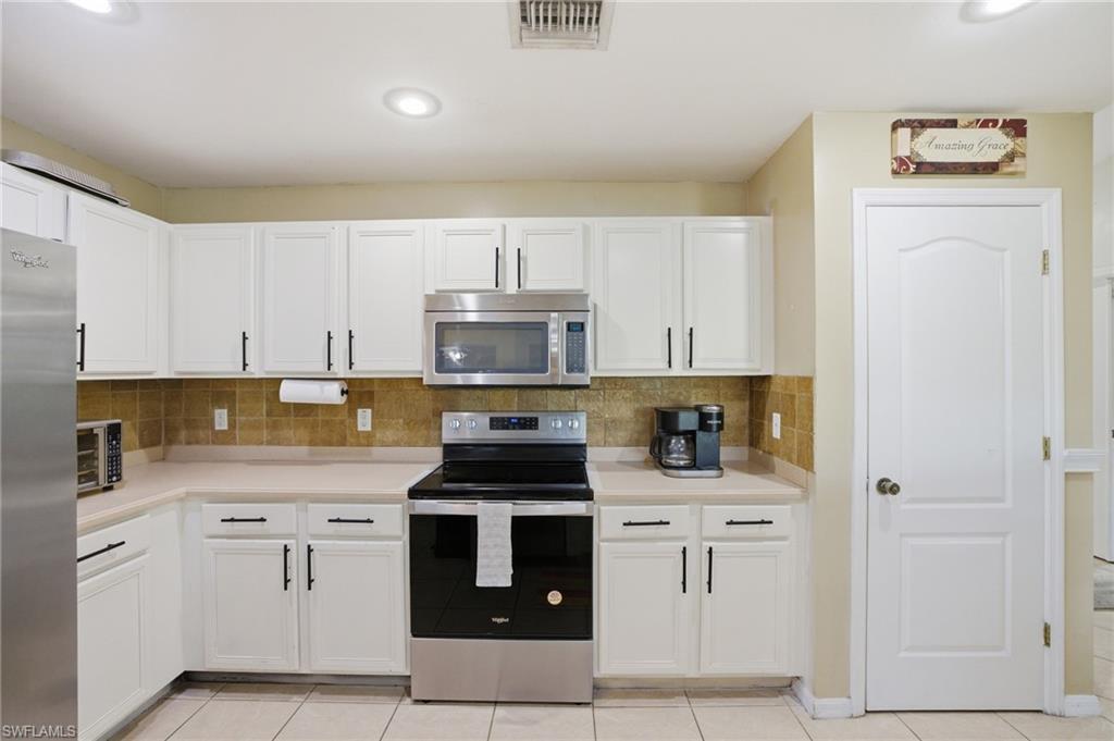 Kitchen featuring stainless steel appliances, white cabinetry, light countertops, and tasteful backsplash
