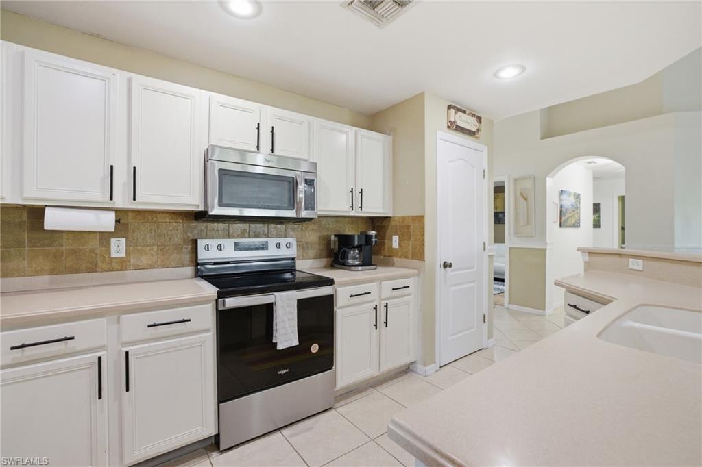 Kitchen featuring stainless steel appliances, light countertops, white cabinets, decorative backsplash, and arched walkways