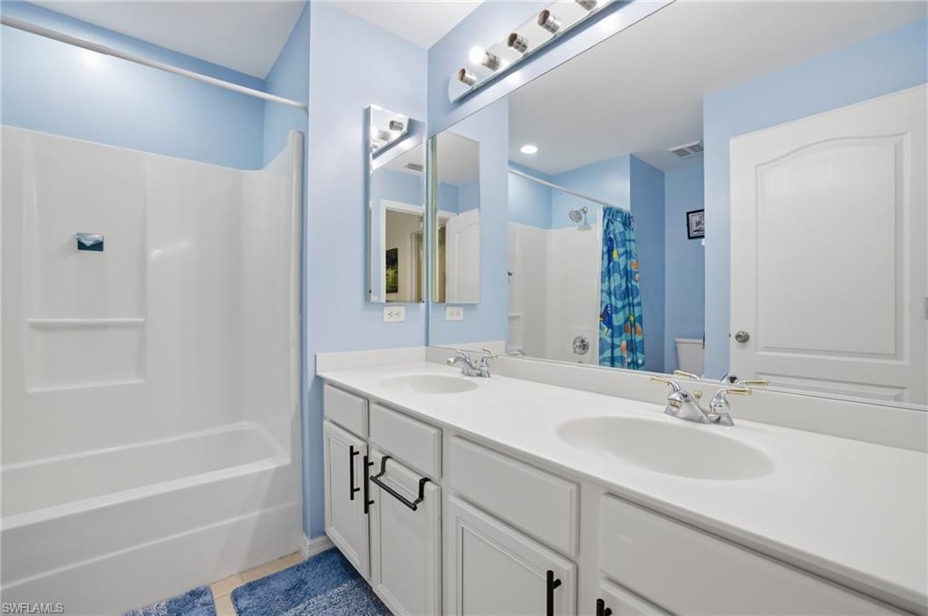 Full bath with double vanity, shower / tub combo with curtain, and light tile patterned floors