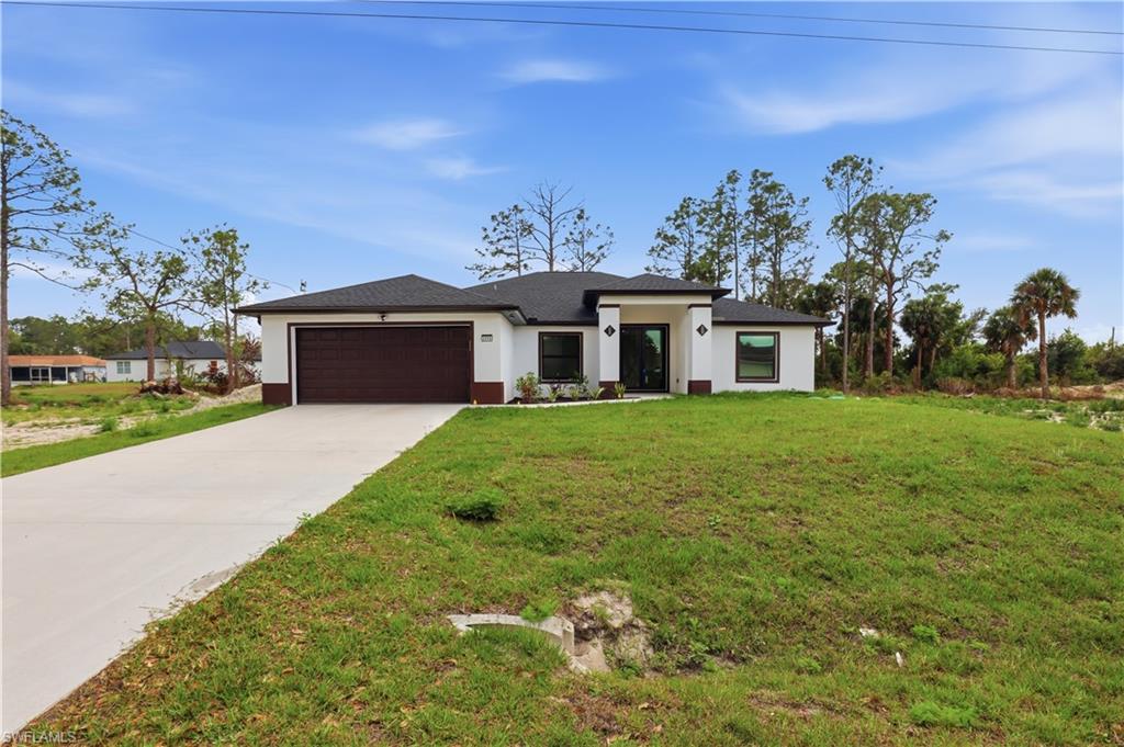Prairie-style house featuring a front lawn, a garage, concrete driveway, stucco siding, and roof with shingles