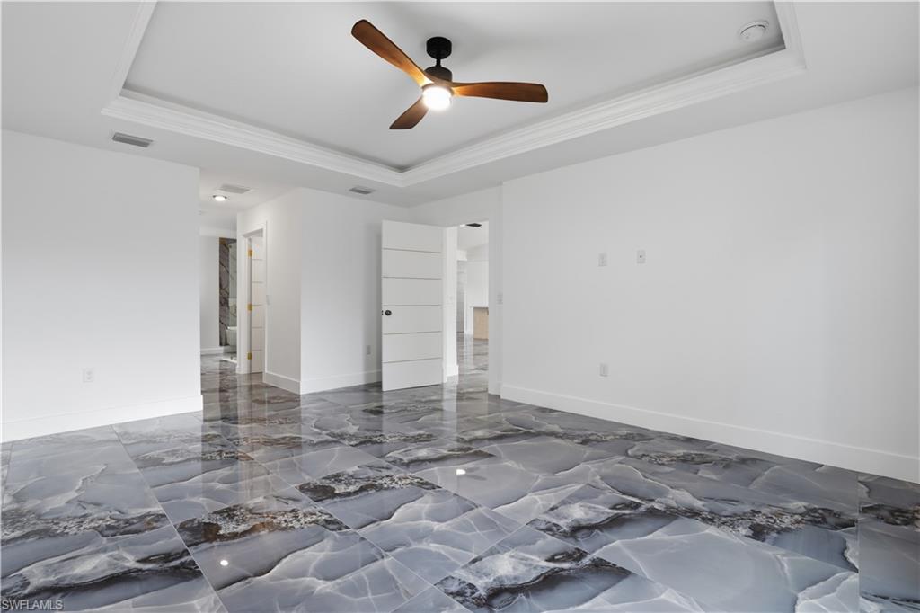 Spare room with a raised ceiling, a ceiling fan, crown molding, and dark marble finish flooring