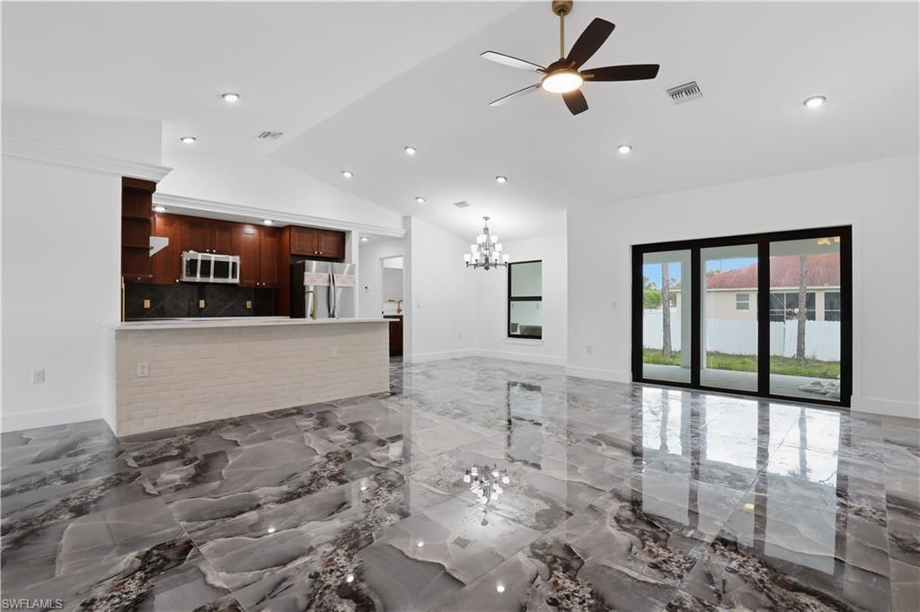 Unfurnished living room with a ceiling fan, suspended lighting, light marble finish floors, and vaulted ceiling