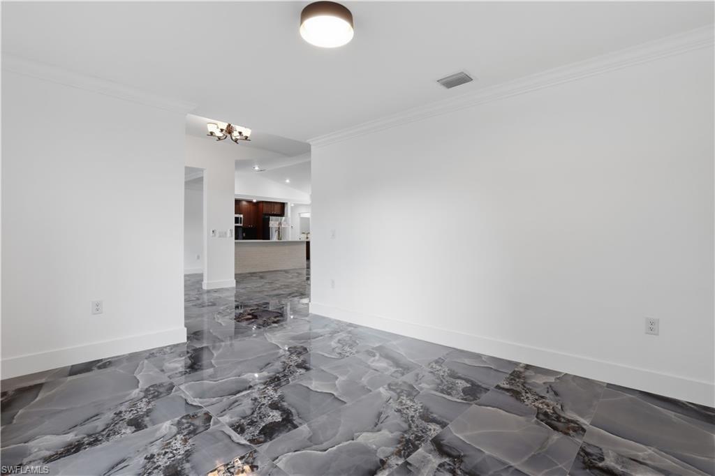 Unfurnished room featuring ornamental molding, dark marble finish flooring, and a chandelier