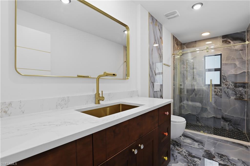 Bathroom featuring vanity, a marble finish shower, recessed lighting, and marble tiled flooring