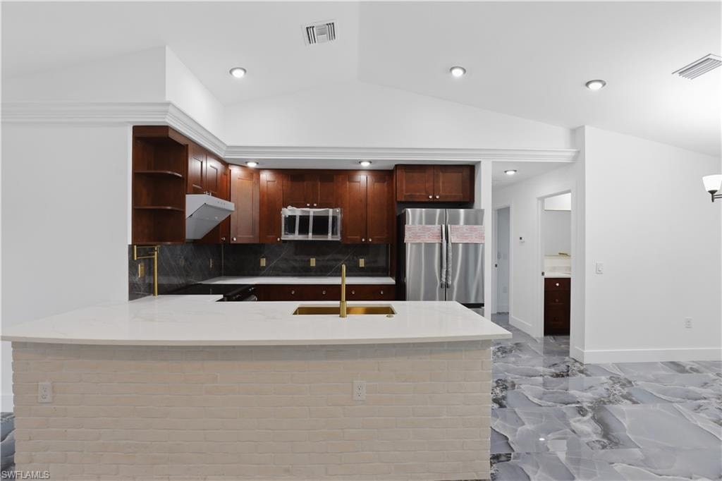Kitchen featuring a peninsula, open shelves, light stone countertops, stainless steel appliances, and vaulted ceiling