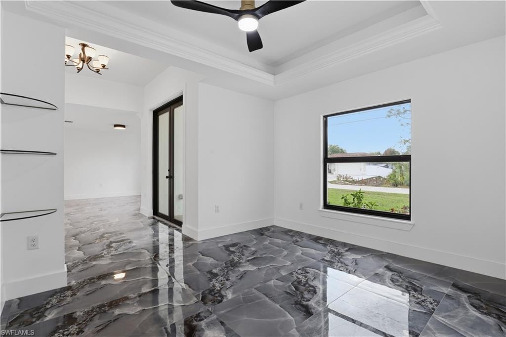 Spare room with dark marble finish floors, ceiling fan, a raised ceiling, suspended lighting, and ornamental molding