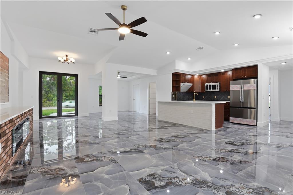 Unfurnished living room with ceiling fan, light marble finish floors, and vaulted ceiling