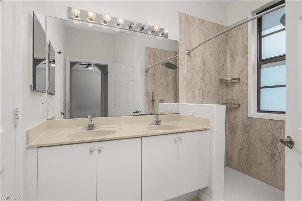 Full bath with double vanity and a marble finish shower