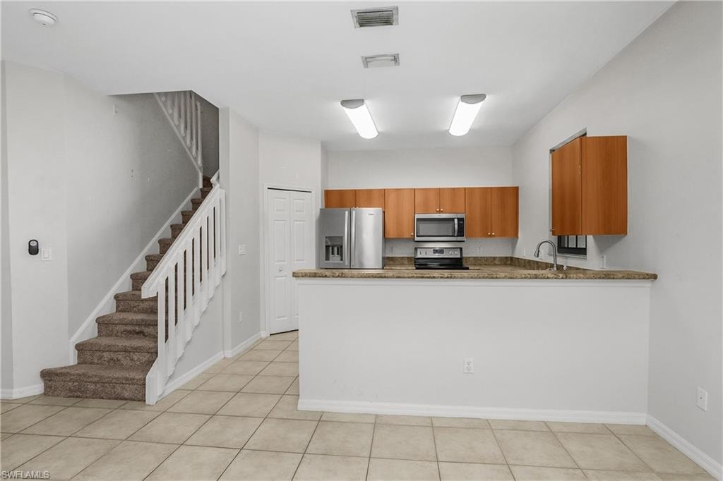 Kitchen featuring wood finish cabinetry, stainless steel appliances, dark stone counters, and a peninsula