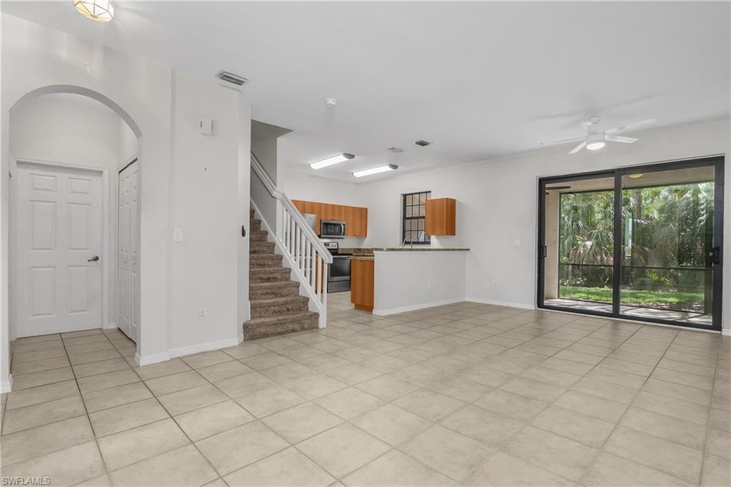 Unfurnished living room featuring ceiling fan, arched walkways, and light tile patterned floors