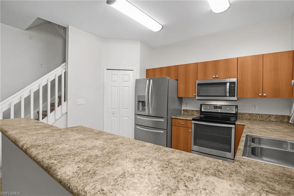 Kitchen with stainless steel appliances, wood finish cabinets, a peninsula, and light stone counters