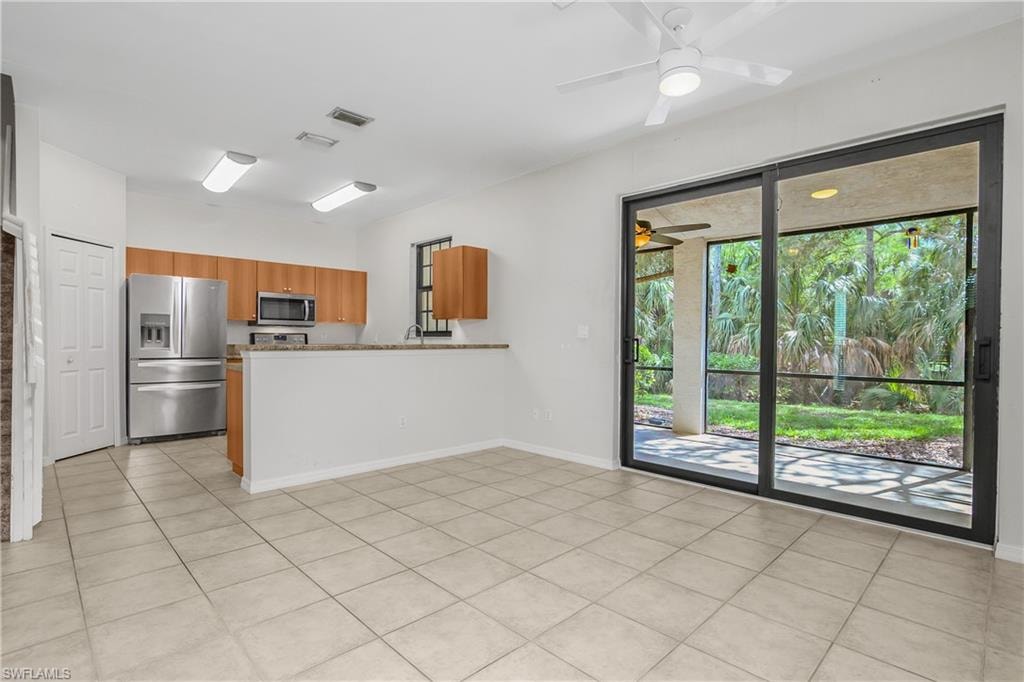 Kitchen featuring stainless steel appliances, wood finish cabinets, a peninsula, a ceiling fan, and light tile patterned floors