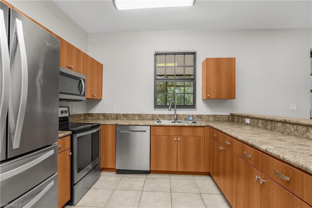 Kitchen with stainless steel appliances, wood finish cabinetry, light tile patterned floors, and light stone countertops
