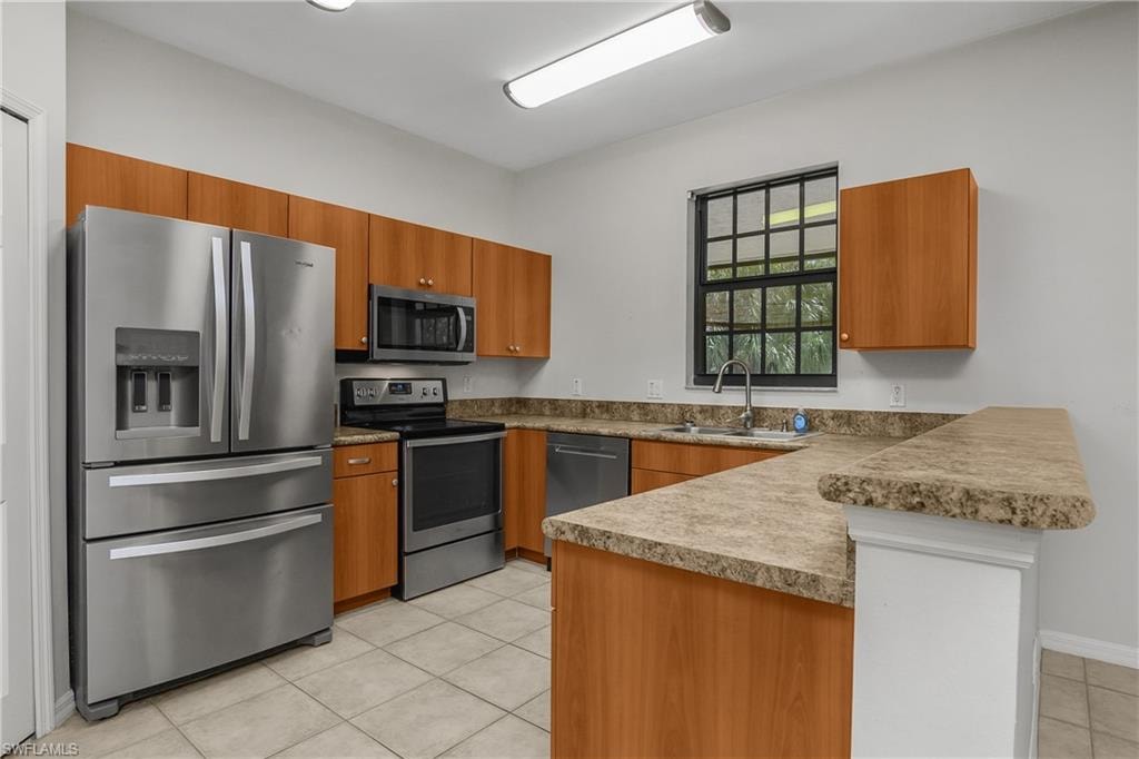 Kitchen featuring stainless steel appliances, a peninsula, wood finish cabinetry, light tile patterned floors, and a kitchen bar