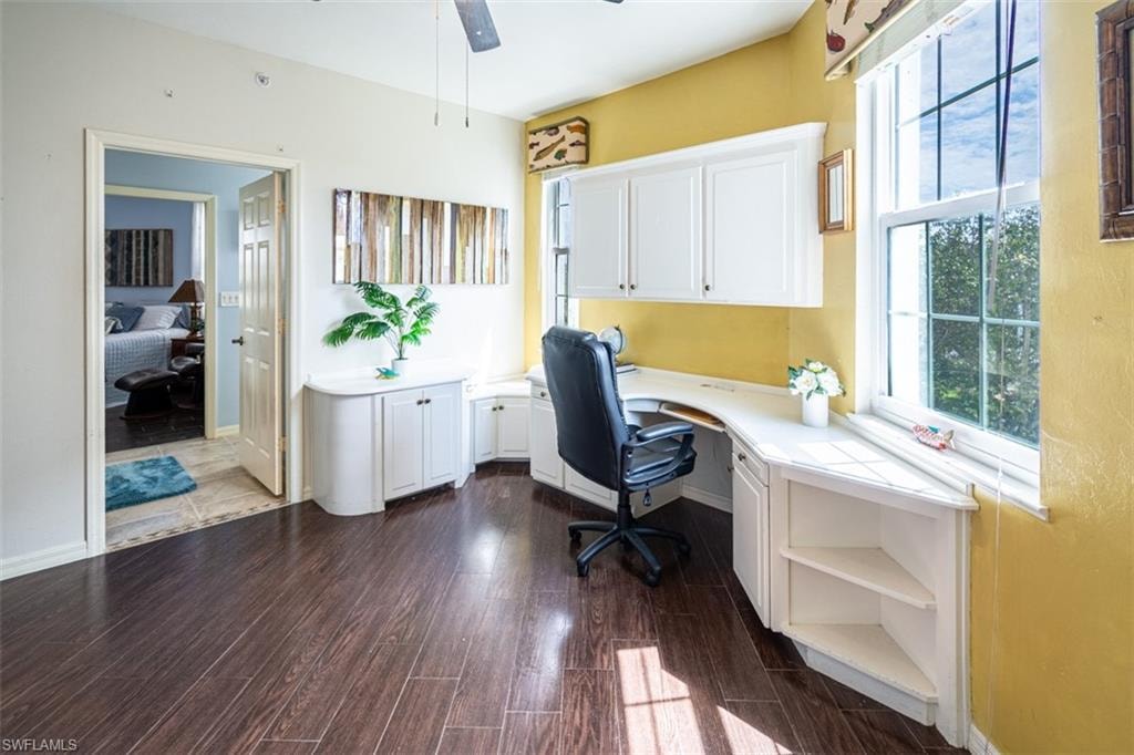 Office area featuring a ceiling fan, dark wood finished floors, and built in desk