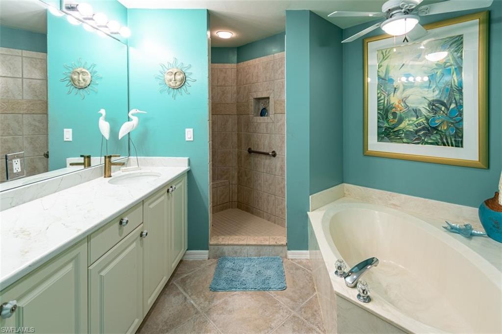 Full bathroom with vanity, a walk in shower, ceiling fan, a garden tub, and light tile patterned flooring