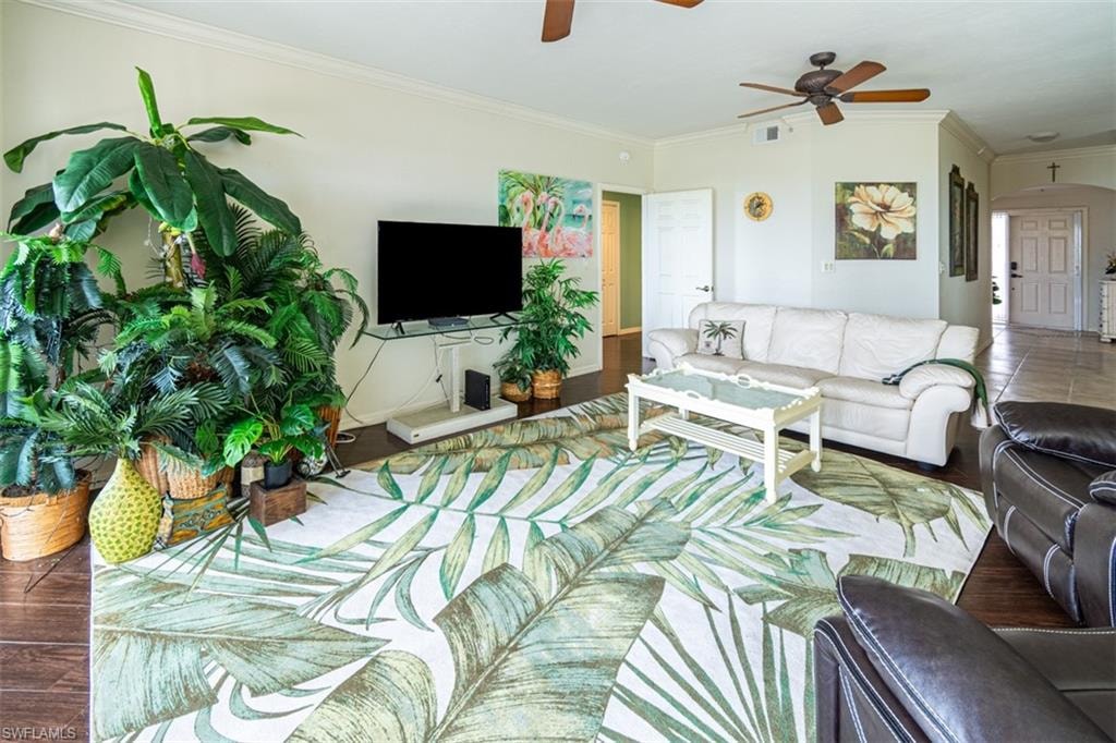 Living room with arched walkways, crown molding, and ceiling fan