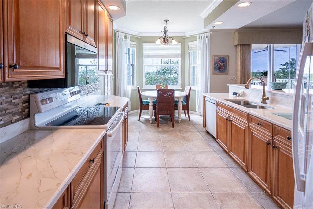 Kitchen with white appliances, crown molding, wood finish cabinets, backsplash, and light stone countertops