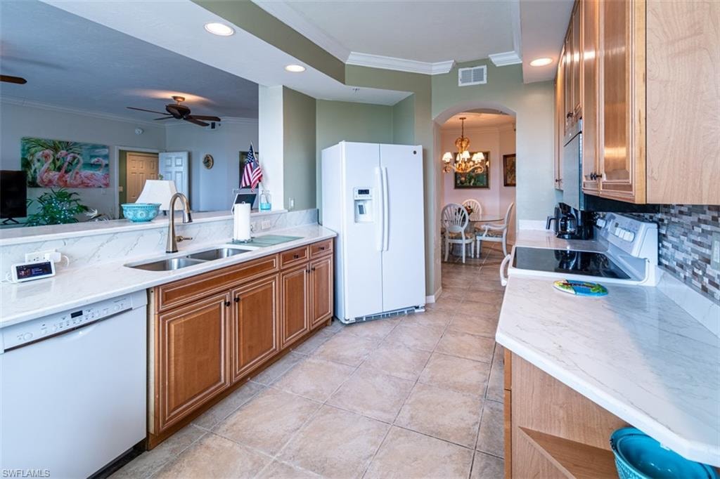 Kitchen featuring crown molding, wood finish cabinetry, white appliances, arched walkways, and tasteful backsplash