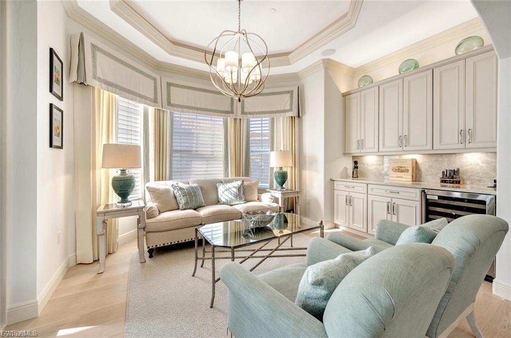 Living area featuring hanging lights, crown molding, wine cooler, light wood-style floors, and a raised ceiling