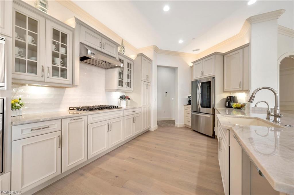 Kitchen featuring crown molding, stainless steel appliances, light wood-style floors, light stone counters, and glass fronted cabinets