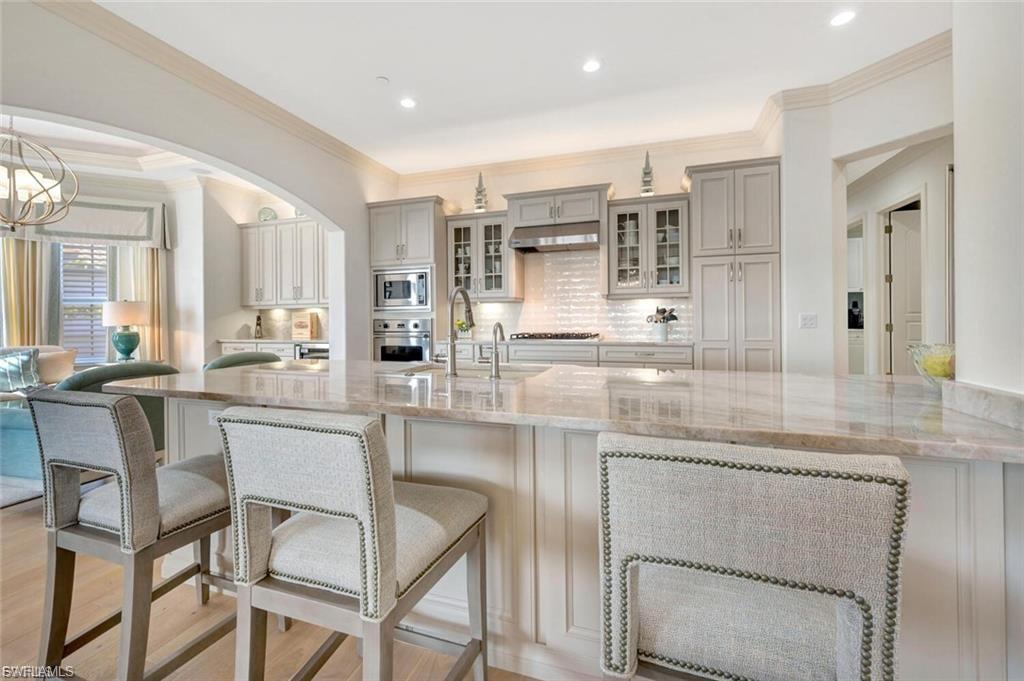 Kitchen with a kitchen breakfast bar, light stone countertops, ornamental molding, glass fronted cabinets, and backsplash