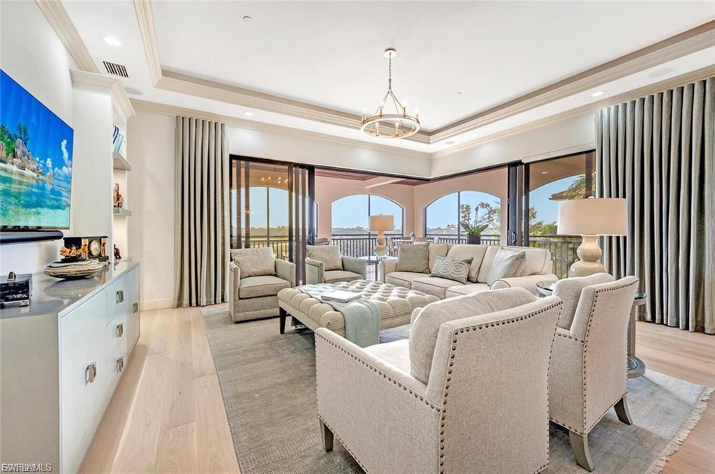 Living room featuring light wood-style flooring, a tray ceiling, suspended lighting, and ornamental molding