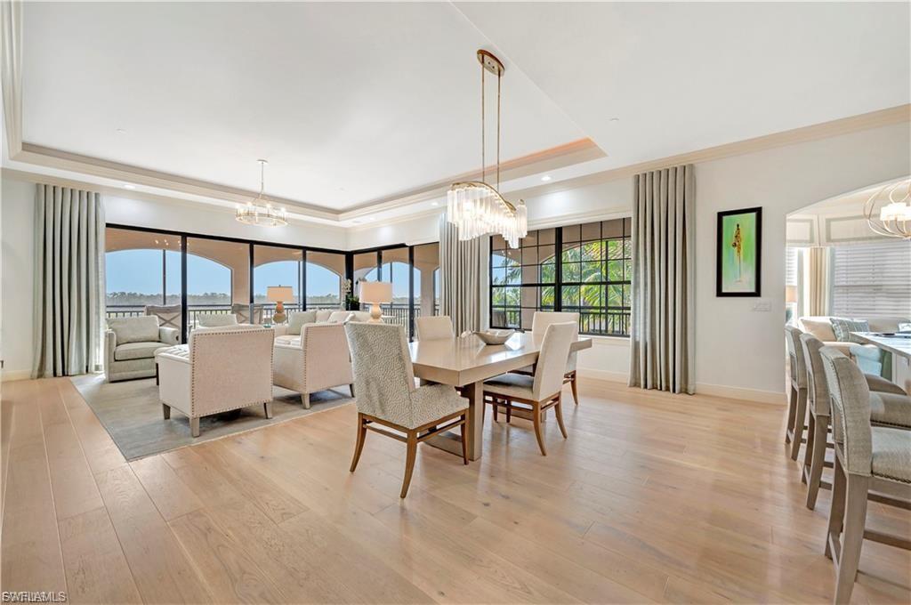 Dining space featuring suspended lighting, crown molding, light wood-type flooring, arched walkways, and a tray ceiling