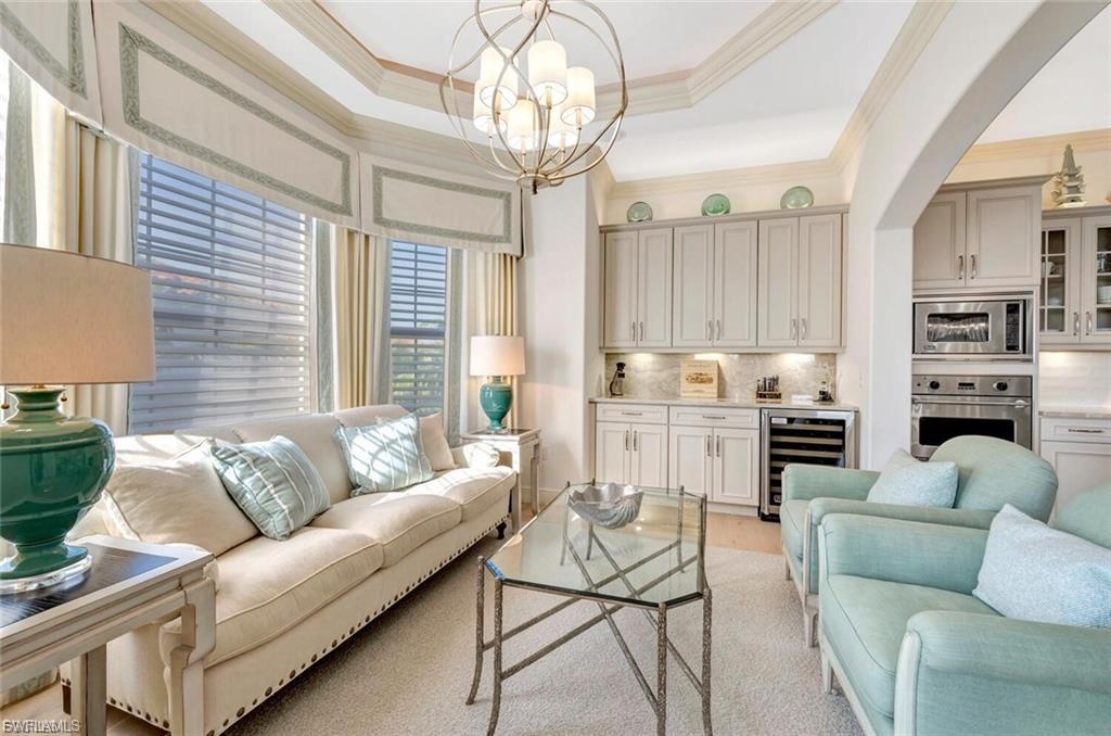 Sitting room with beverage cooler, suspended lighting, ornamental molding, and light wood-type flooring