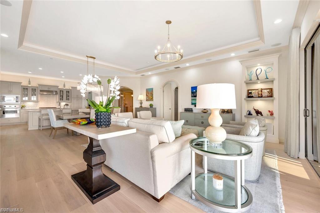 Living area with arched walkways, hanging lights, light wood-type flooring, a tray ceiling, and crown molding