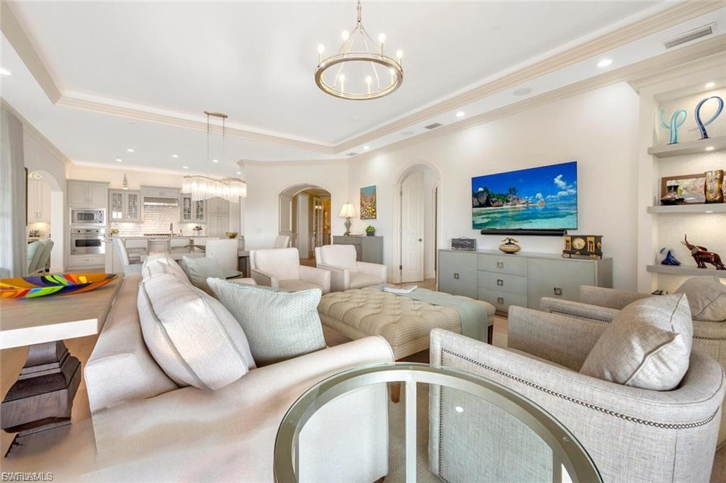 Living room with arched walkways, a chandelier, ornamental molding, and a tray ceiling