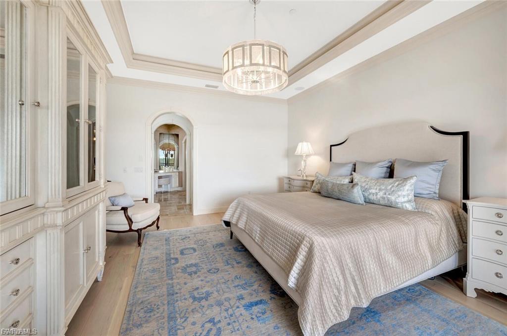 Bedroom with arched walkways, a tray ceiling, light wood-type flooring, hanging lights, and ornamental molding