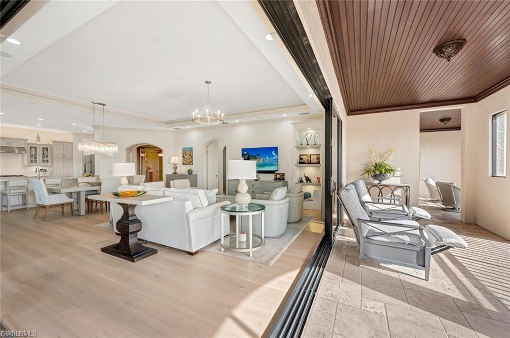 Living room featuring arched walkways, suspended lighting, crown molding, and stone tile floors