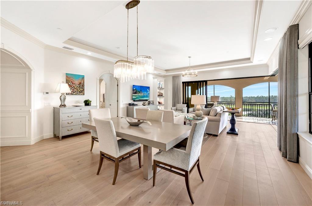 Dining room with hanging lights, ornamental molding, arched walkways, light wood finished floors, and a tray ceiling