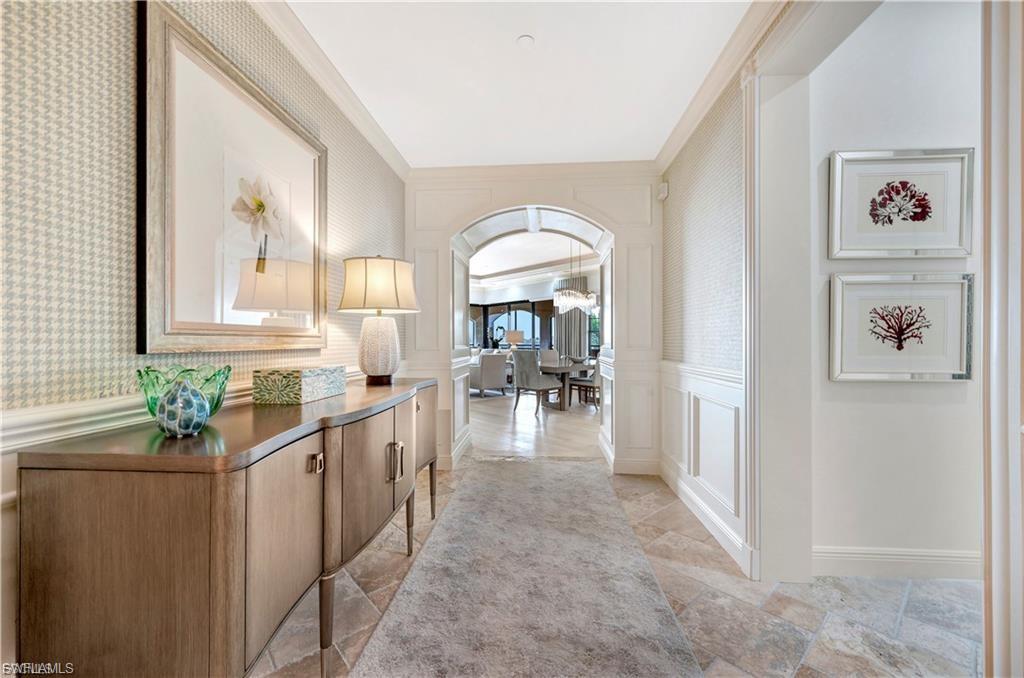 Hall featuring a decorative wall, arched walkways, wallpapered walls, a wainscoted wall, and crown molding