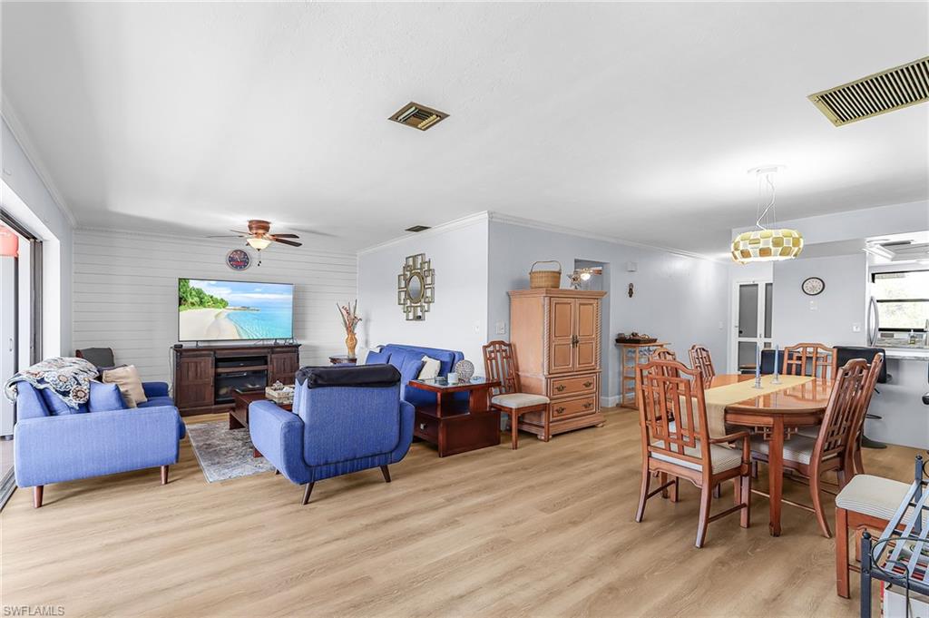 Dining room with light wood finished floors, ornamental molding, ceiling fan, and wooden walls