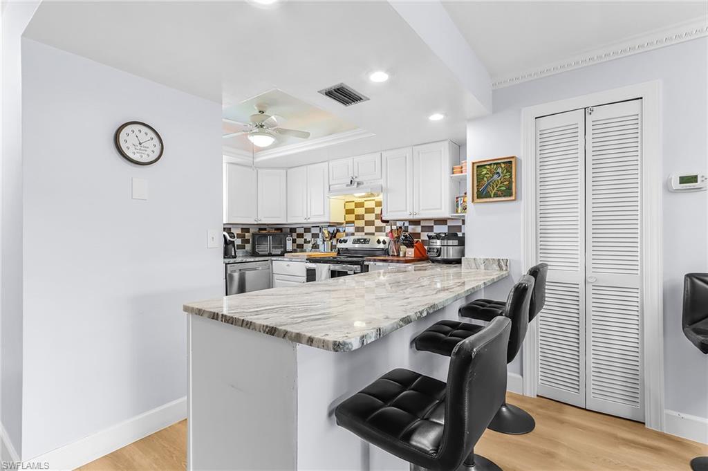 Kitchen with a tray ceiling, tasteful backsplash, light wood finished floors, a kitchen bar, and a peninsula