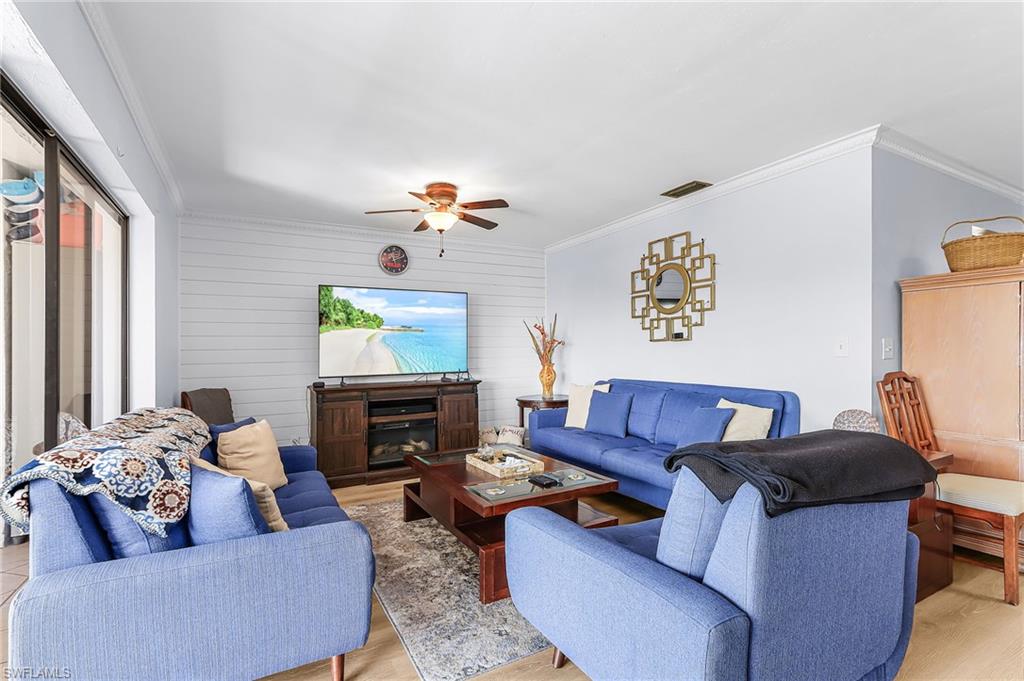 Living room featuring ornamental molding, wood walls, light wood-style flooring, a glass covered fireplace, and a ceiling fan