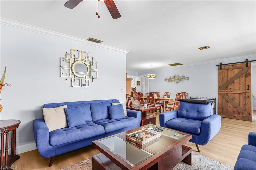 Living area with a barn door, ornamental molding, wood finished floors, and ceiling fan