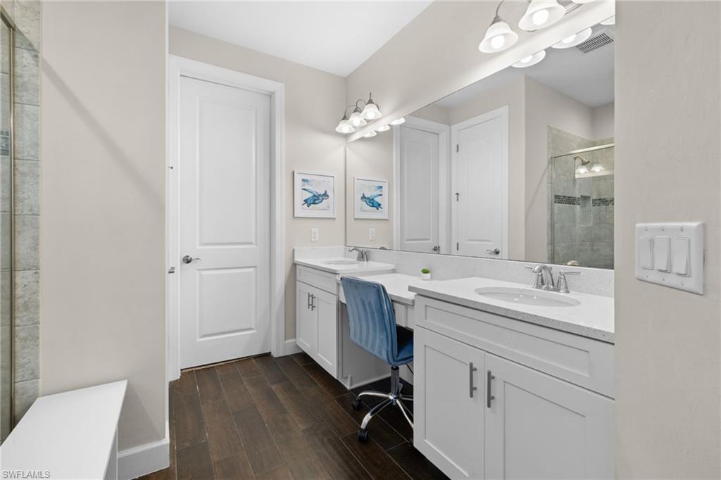 Bathroom featuring a shower stall, double vanity, and dark wood finished floors