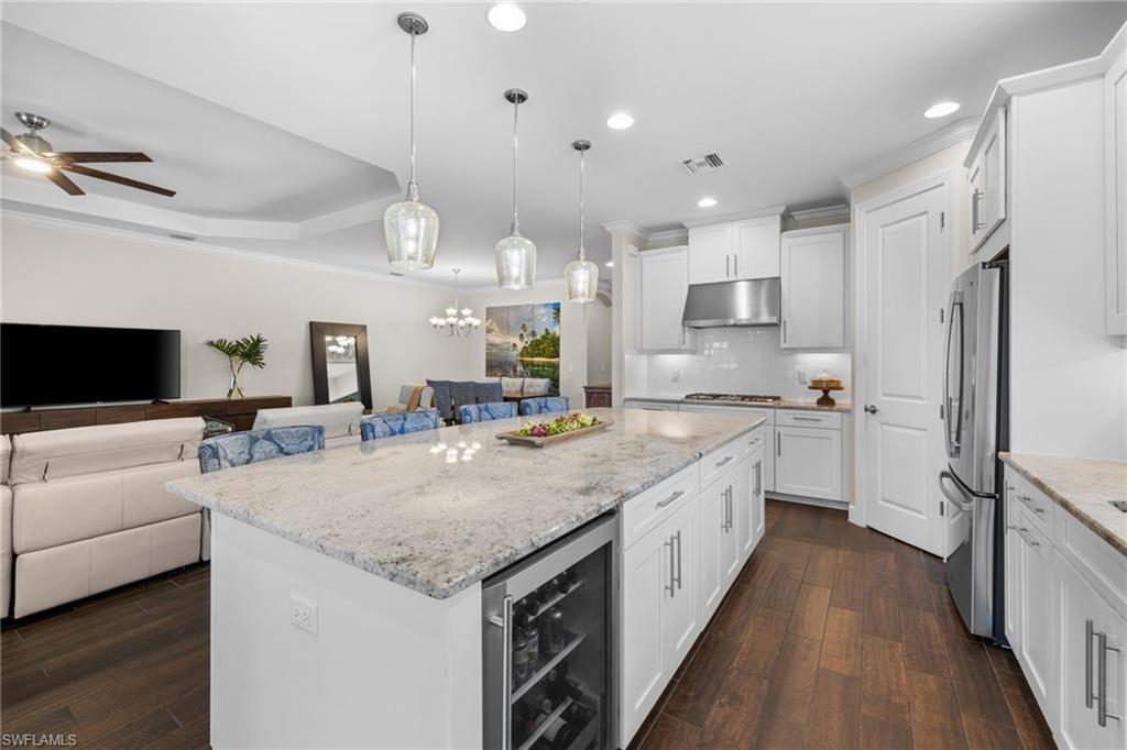 Kitchen featuring open floor plan, white cabinets, beverage cooler, light stone countertops, and dark wood-style floors