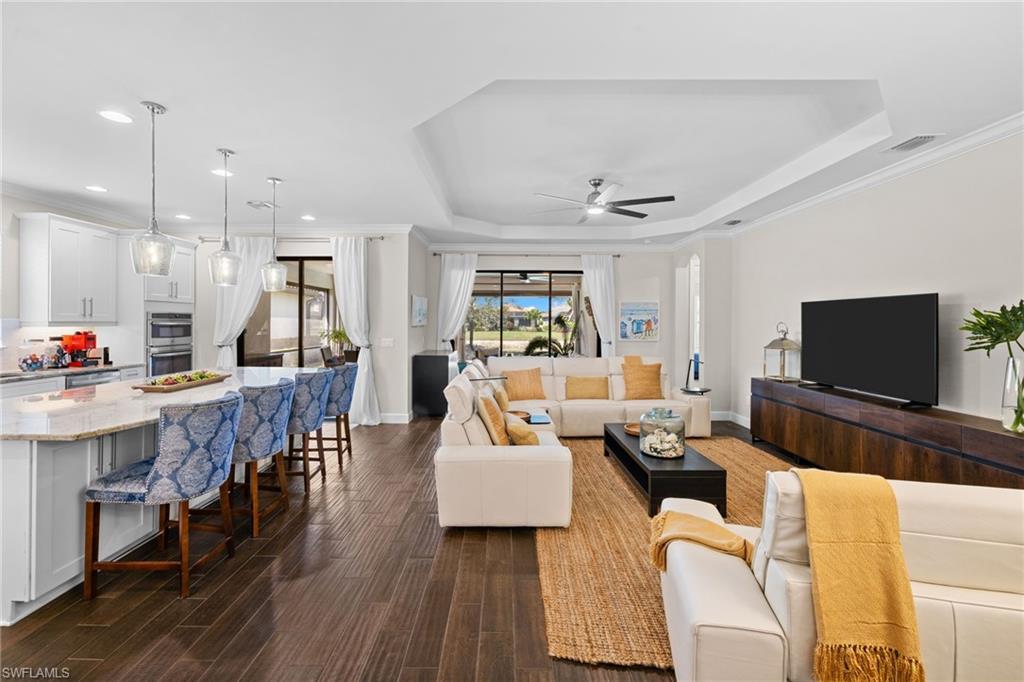 Living area featuring crown molding, a ceiling fan, dark wood-style flooring, a tray ceiling, and recessed lighting