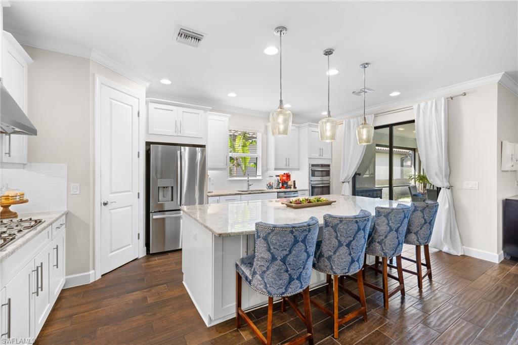 Kitchen featuring a breakfast bar area, white cabinets, dark wood finished floors, light stone countertops, and stainless steel appliances