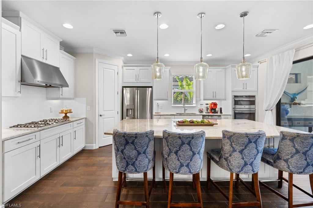 Kitchen with white cabinetry, light stone counters, ornamental molding, a kitchen bar, and stainless steel appliances