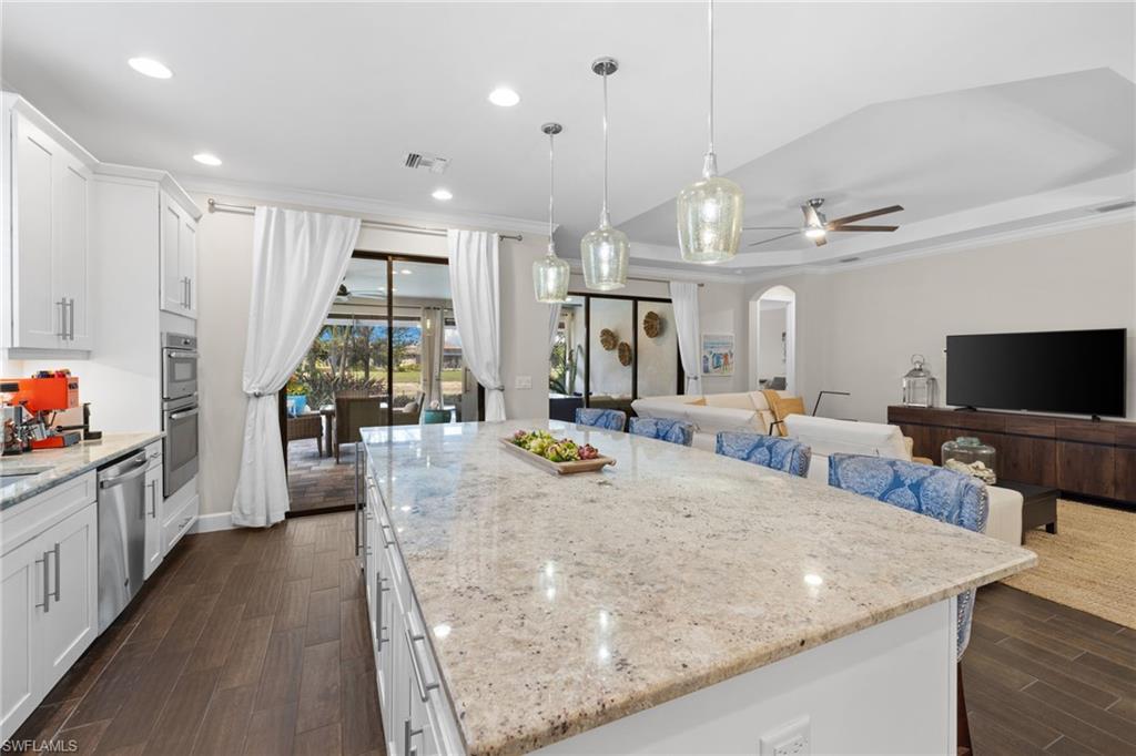 Kitchen with white cabinetry, light stone countertops, arched walkways, dark wood-style floors, and ornamental molding