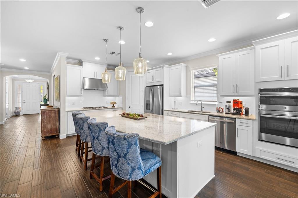 Kitchen featuring backsplash, arched walkways, a kitchen bar, crown molding, and white cabinetry