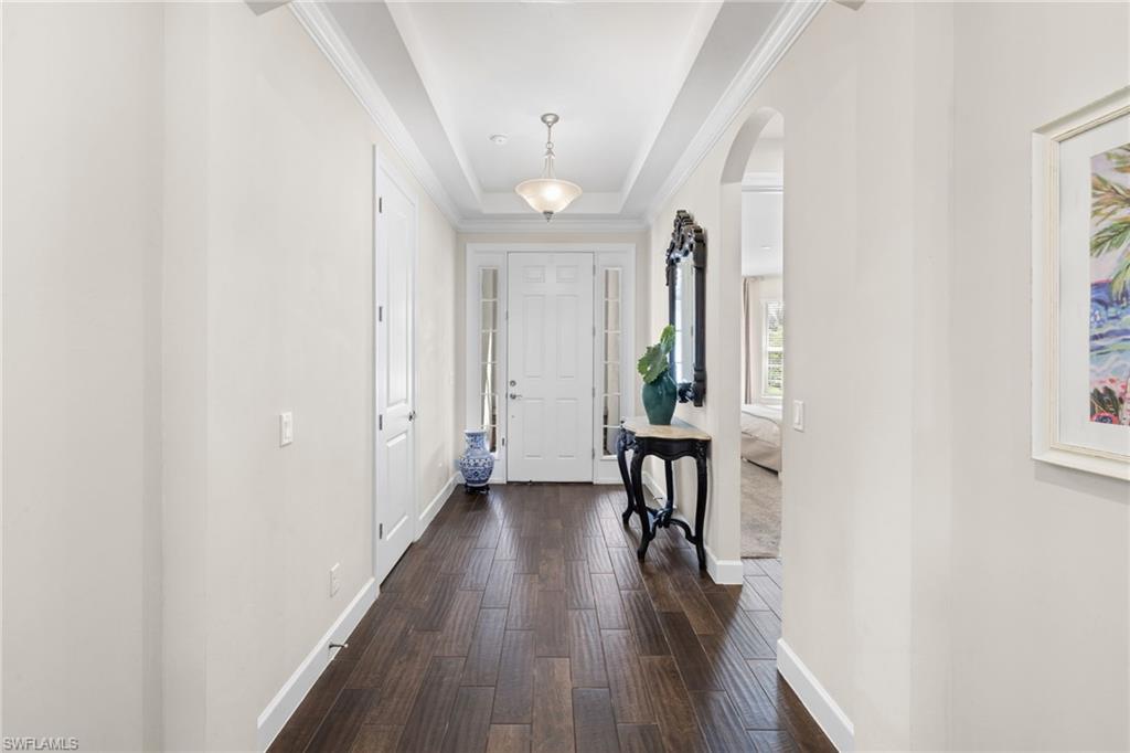 Foyer entrance featuring a raised ceiling, arched walkways, and dark wood finished floors