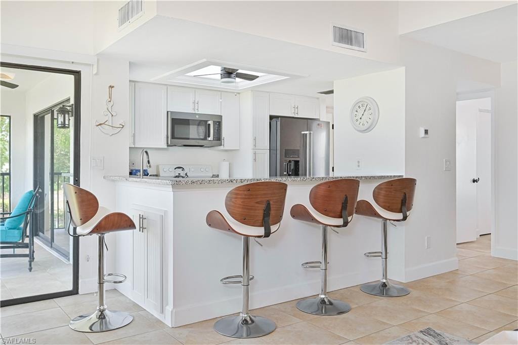 Kitchen featuring a breakfast bar area, stainless steel appliances, light stone countertops, white cabinets, and a ceiling fan