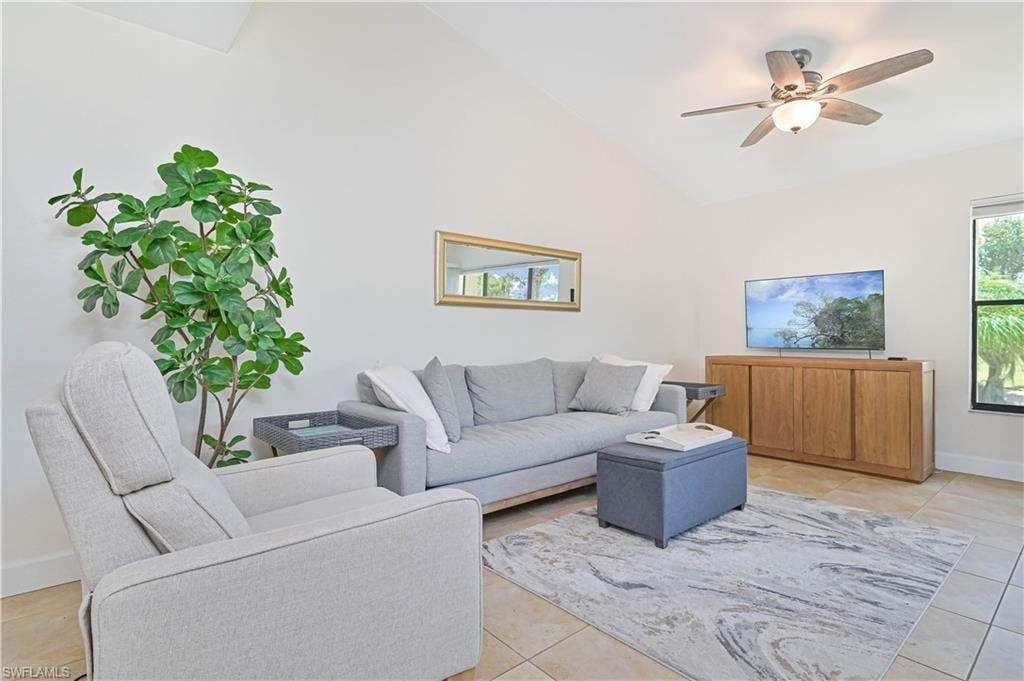 Living room with ceiling fan, light tile patterned floors, and lofted ceiling
