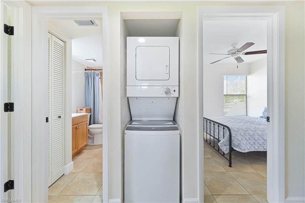 Laundry area with stacked washer and clothes dryer, light tile patterned flooring, and a ceiling fan